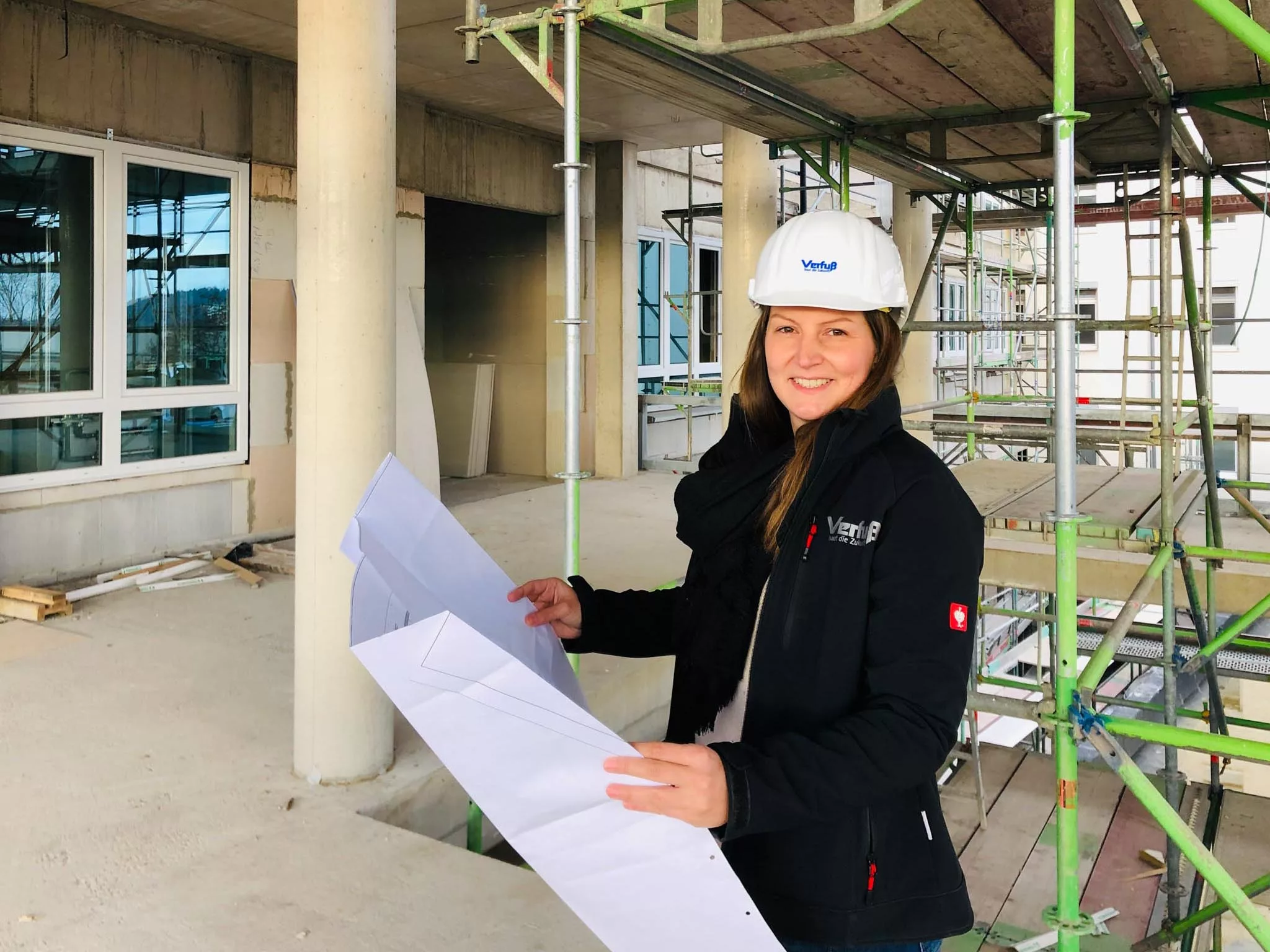 Bauleiterin steht in einer Baustelle prüft anhand eines Plans den Stand eines Bauprojekts